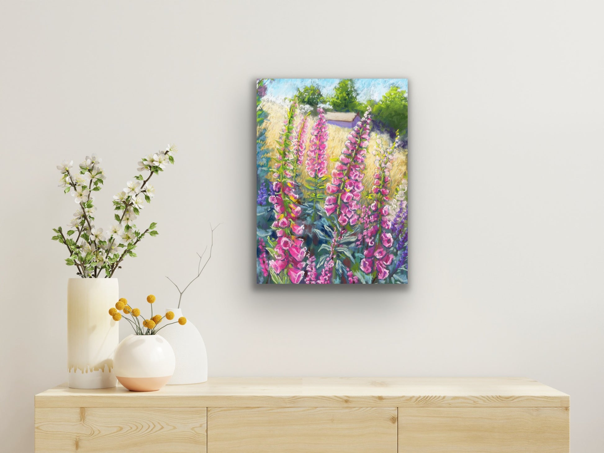 Pink foxgloves in the foreground with a field and building in the background landscape