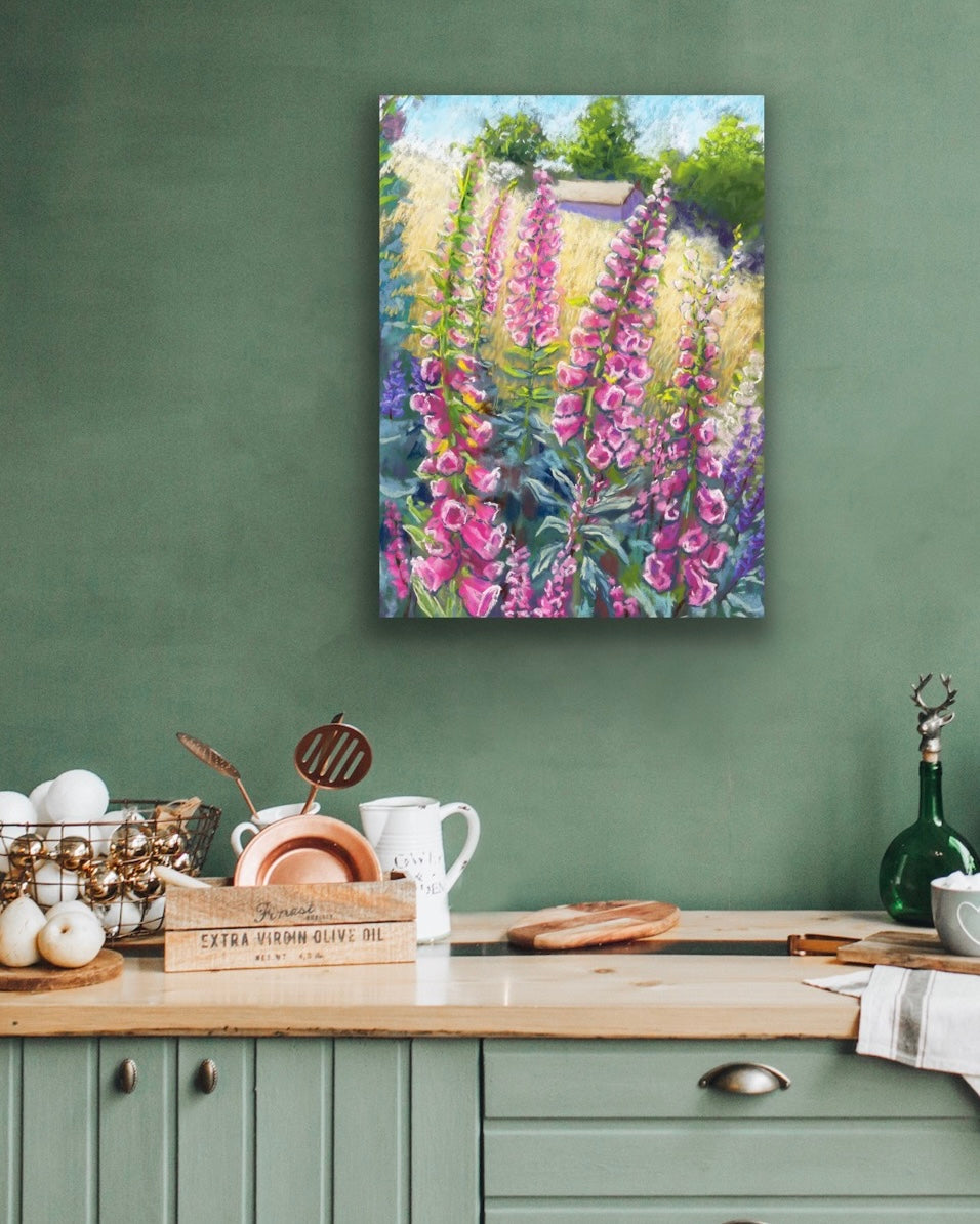 Pink foxgloves in the foreground with a field and building in the background landscape