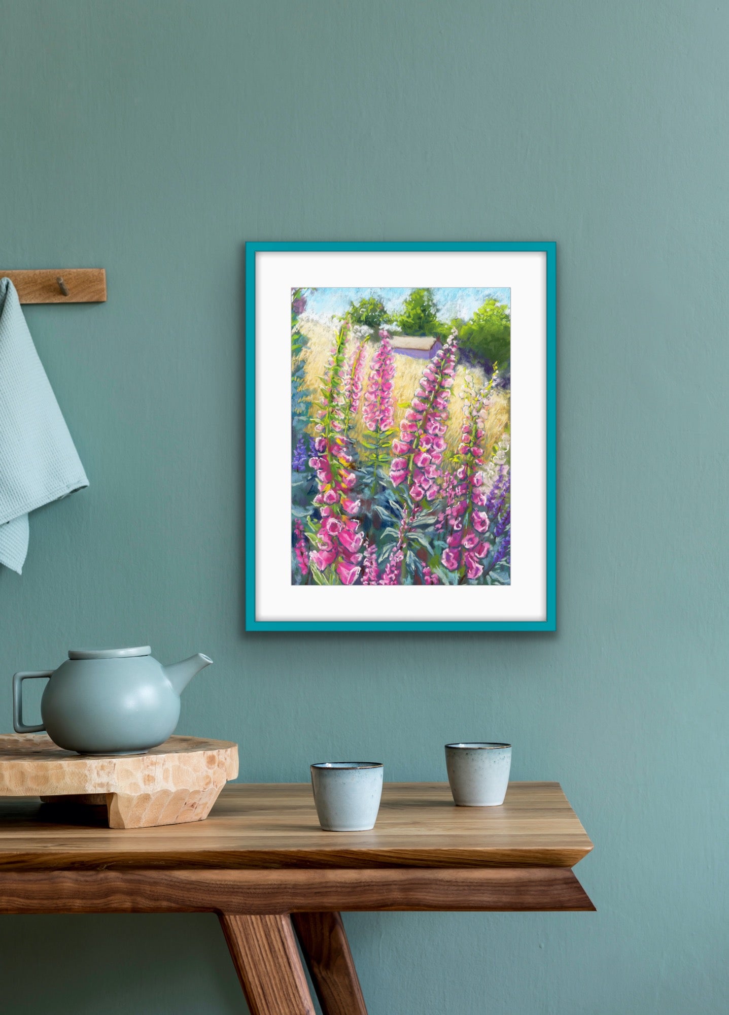 Pink foxgloves in the foreground with a field and building in the background landscape