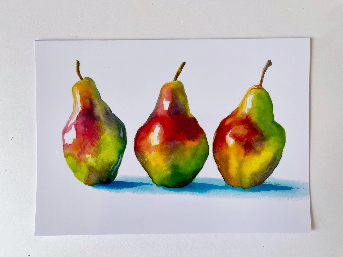 A trio of pears stand in a row, alongside each other. They are brightly coloured in greens, reds, yellows and purples and painted in a stylised manner so the colours bleed into each other. The shadows cast are depicted in a vibrant turquoise blue.